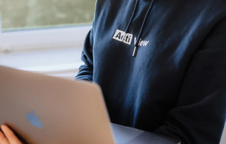 Webentwickler in einem dunkelblauen Hoodie mit der Aufschrift 'ActiView', die an einem silbernen Laptop arbeitet.