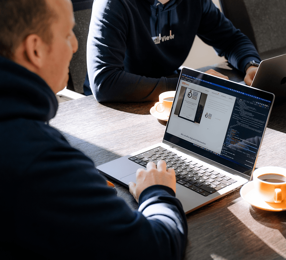 Webentwickler in einem dunkelblauen Hoodie mit der Aufschrift 'ActiView', die an einem silbernen Laptop arbeitet.